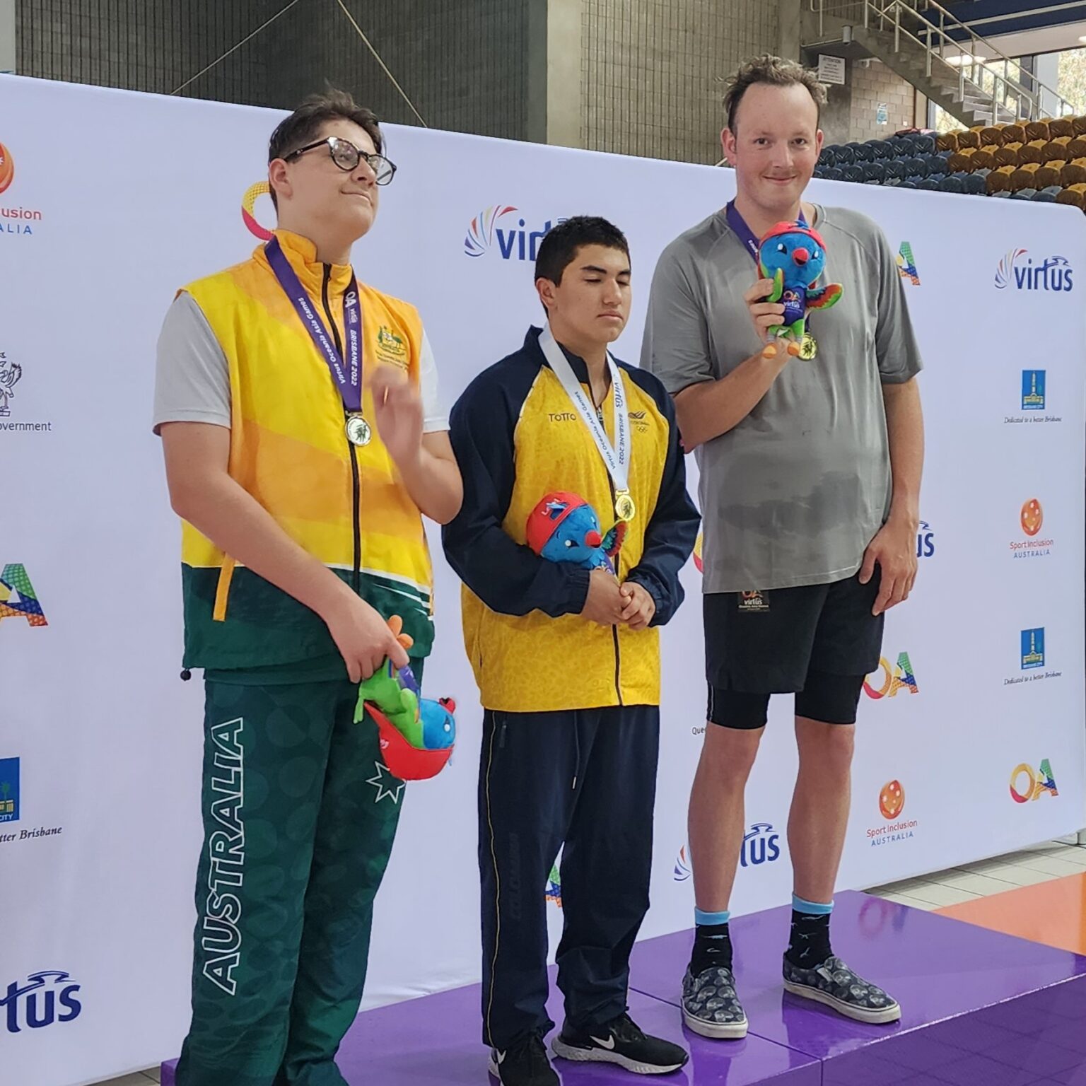 Tate Pichon on podium with two other athletes, holding up medal