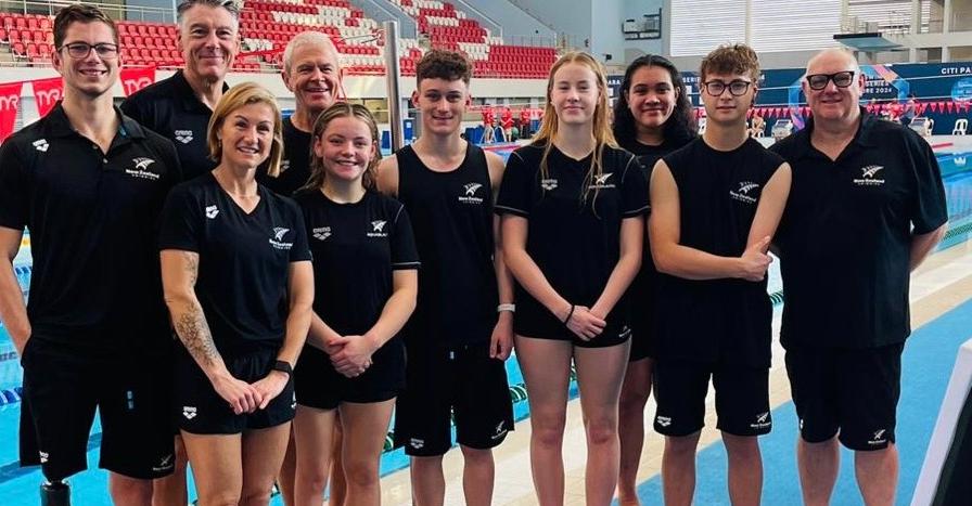 10 Adults stand for a group photos on the side of a indoor swimming pool